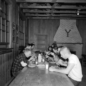 White men eating meal at table with letter "Y" mounted brick fireplace in background