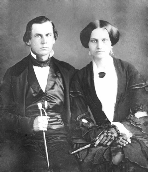 White man in suit and vest holding a cane with white woman in dress and gloves