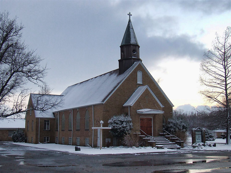 Brick church building with steeple in winter with sign and parking lot