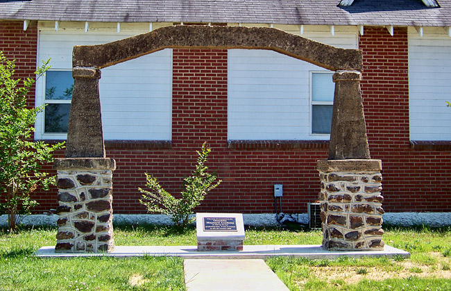 stone arch over small brick base with plaque in front of siding and brick building