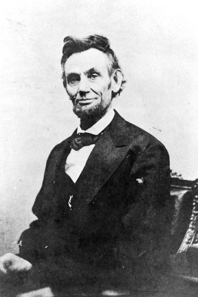 Portrait bearded white man seated at desk smiling disheveled hair suit bow tie