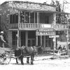 White man in a hat with horse drawn wagon pulling up to two-story building