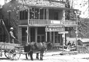 White man in a hat with horse drawn wagon pulling up to two-story building