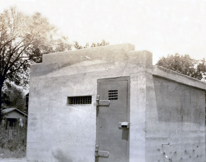Single-story building with small barred window and metal door