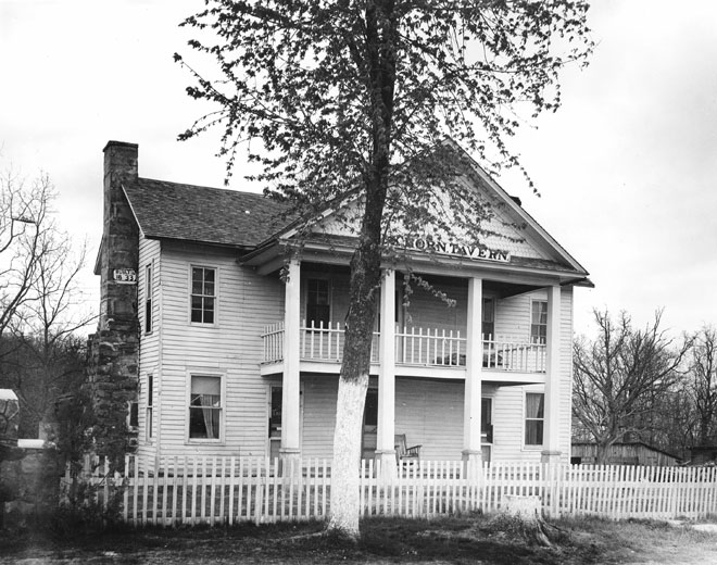 Two-story structure with brick chimney, white picket fence, and tree beyond the fence