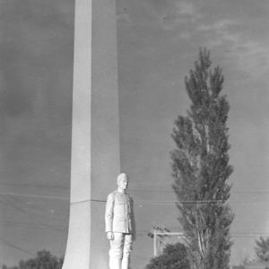 Tall obelisk with statue of soldier and plaque with trees in the background