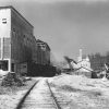 Tall narrow building and railroad tracks with train cars and mill