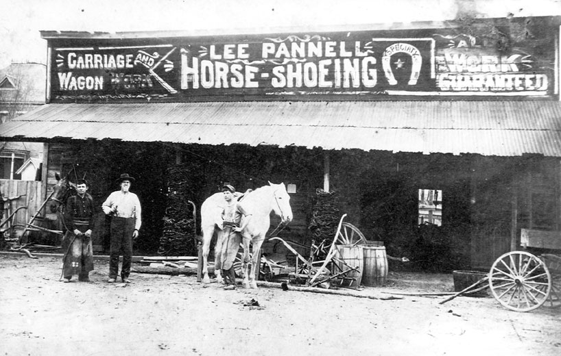 White man and women with horse in front of "Lee Pannell Horse Shoeing" shop
