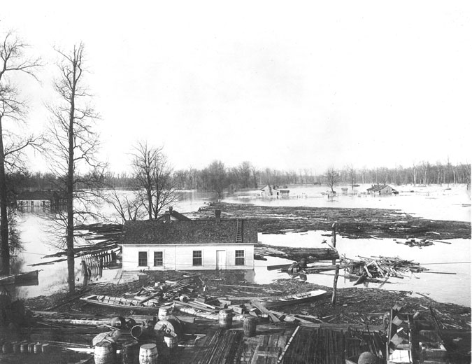 Houses in flooded fields with trees and debris