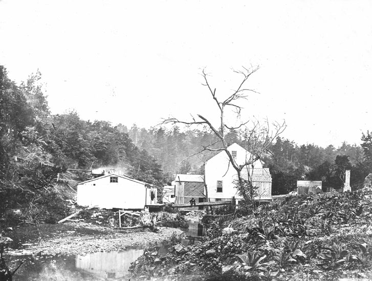 Wooden buildings positioned alongside steam with trees in the background