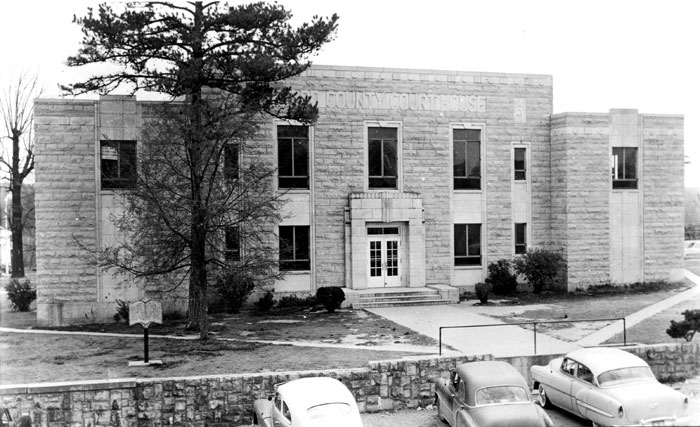 Two-story brick building with stone wall and parked cars in front
