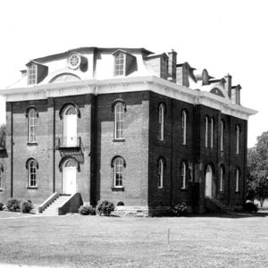 Three-story brick building with single-story expansion, arched windows and arched doorways