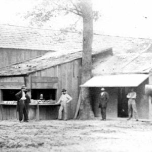 White men in hats with horse outside wooden building