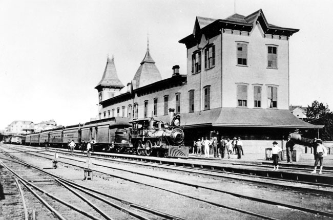 Steam locomotive with cars parked at a two-story train station