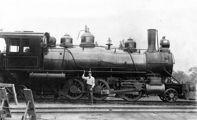 White engineer posing, standing with hand on locomotive