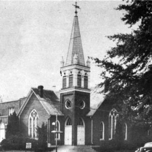 Brick church with spire, arched stain glass, corner entrance, cars, trees