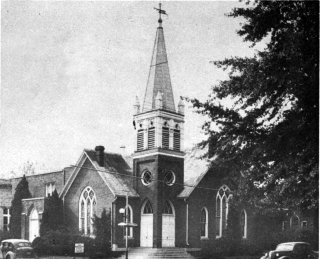 Brick church with spire, arched stain glass, corner entrance, cars, trees