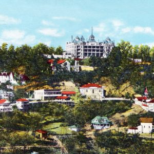Hand tinted photograph hillside town with large hotel on peak