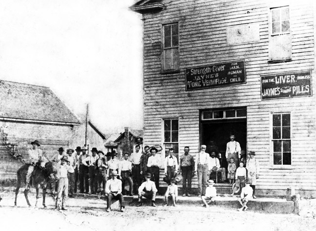 Group photo men children mule outside two-story wooden building with signs "Jayne's tonic vermifuge"