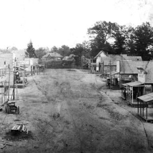 Street scene overhead view with wood frame buildings, porches, building construction, stack of boards, man on ladder