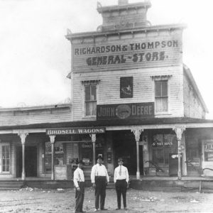 Three white men in hats and ties in front of general store