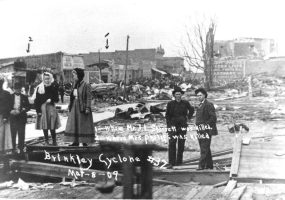White women and men with damaged buildings behind them, photograph labeled "Brinkley Cyclone"