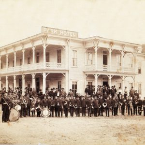 Group photograph of band members "Harrison Band" with onlookers on ornate porch of wood frame "Park Hotel"