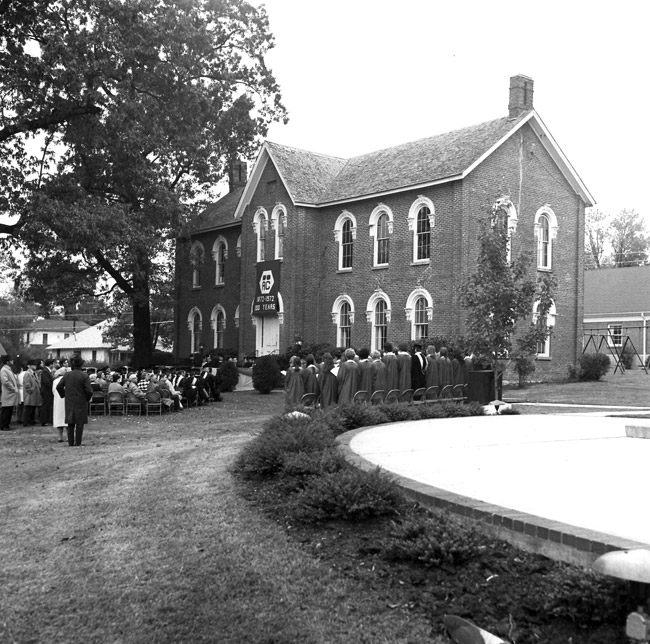 Audience and choir outside two-story brick building with "AC" logo banner reading "1872-1972 100 years"