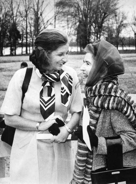 Two white women with scarves chat and laugh in park by river