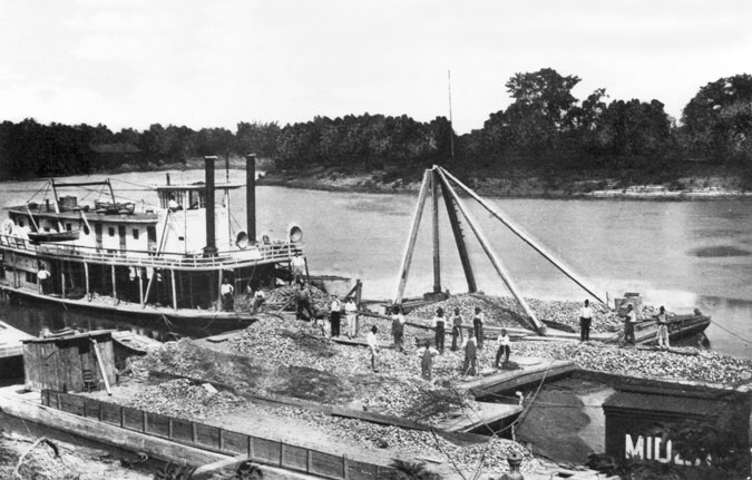 Riverboat and multiple flat barges against riverbank carrying material and  workers