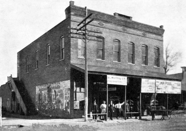 Two story brick building "Alma Drug Co." with onlookers, horse and carriage, faded "Ringling Bros" wall print
