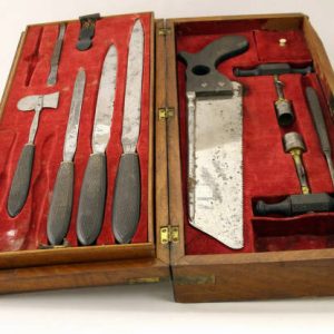 open wooden box with red lining filled with a saw and various knives and other smaller tools