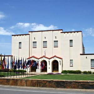 two story white southwestern style building with two rows of flag flanking walkway leading to entrance