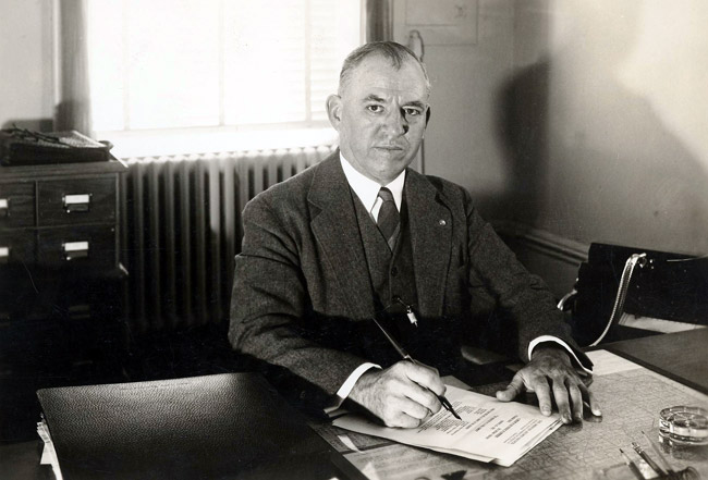 Portrait white man in suit at office desk posing signing document