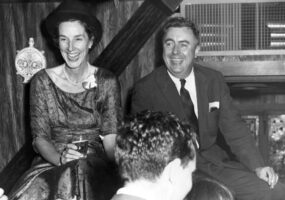 White man and woman formal dress laughing at party with two white people foreground