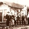 Group of white men and boy in suits and hats standing on railroad tracks at train station