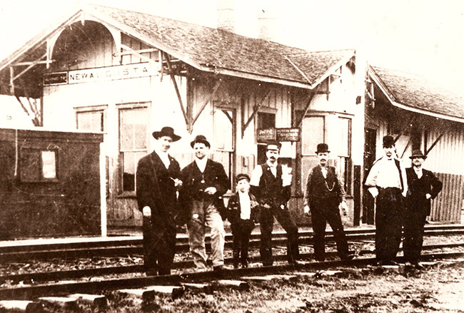 Group of white men and boy in suits and hats standing on railroad tracks at train station