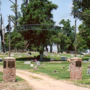 Arched entrance to cemetery with gravestones, trees behind it