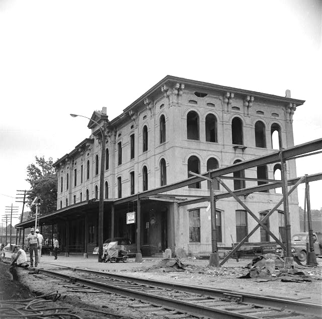 Construction workers on railroad tracks by incomplete three story arched window building