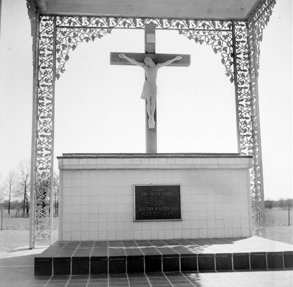 Memorial with crucifix and Jesus figure over tile base with plaque and wrought iron detailed floral columns