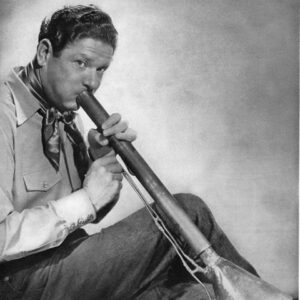 white man dressed as cowboy blowing into long, tubular musical instrument