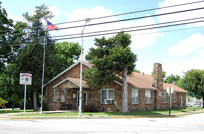 Single-story building with stone walls sign flagpole and tree in front