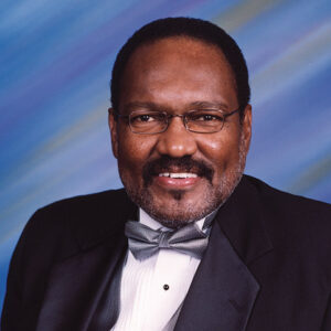 African-American man with glasses and mustache smiling in suit and bow tie
