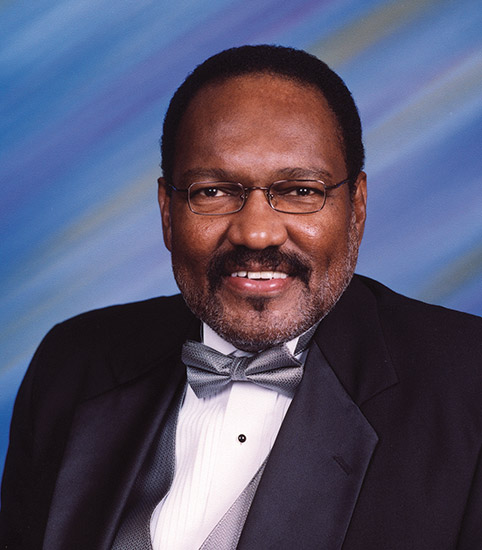 African-American man with glasses and mustache smiling in suit and bow tie