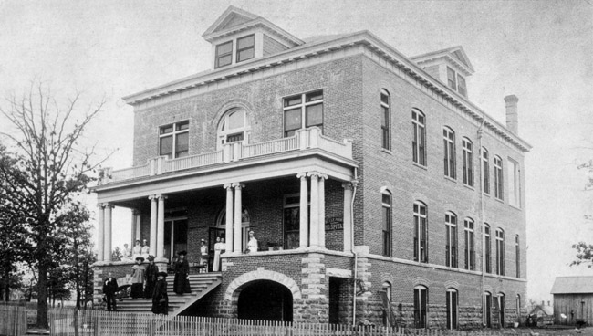 three story brick building with people on front steps and porch