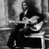 African-American man in suit sitting on a bench playing guitar