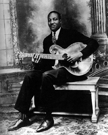 African-American man in suit sitting on a bench playing guitar