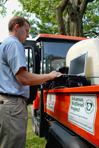 white man using laptop stands at back of utility truck labeled "Arkansas Biodiesel Project"
