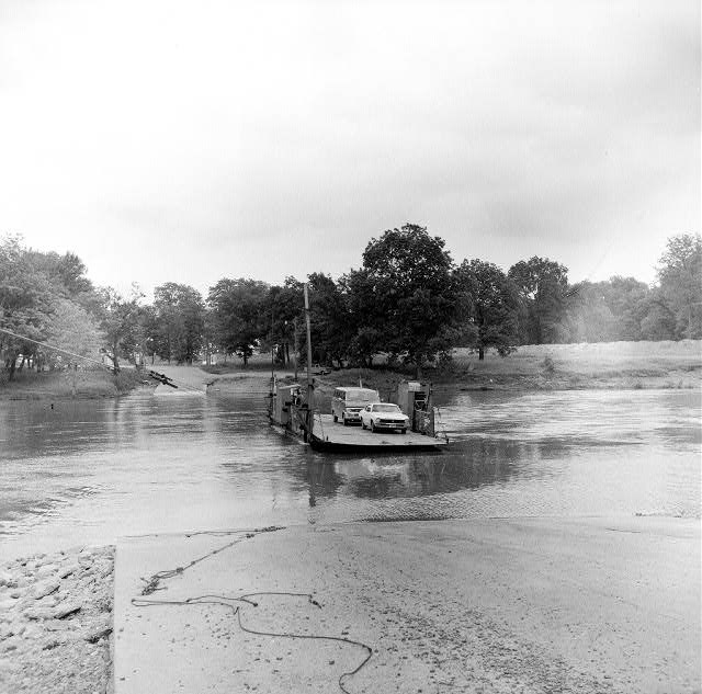 River with ferry approaching ramp carrying car and van field trees road in background