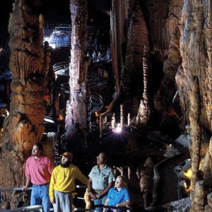 Interior of a large cave with rock formations and tourists walking along a paved path with railings